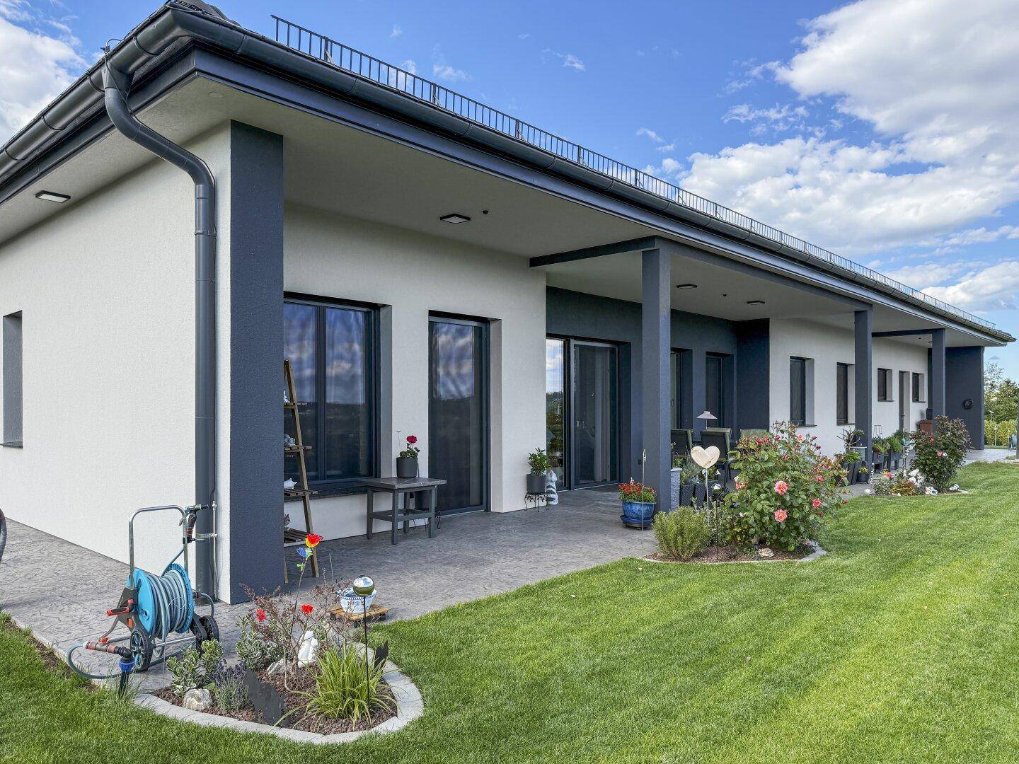 Moderne Terrasse mit Gartenmöbeln und gepflegtem Rasen, umgeben von Blumenbeeten.