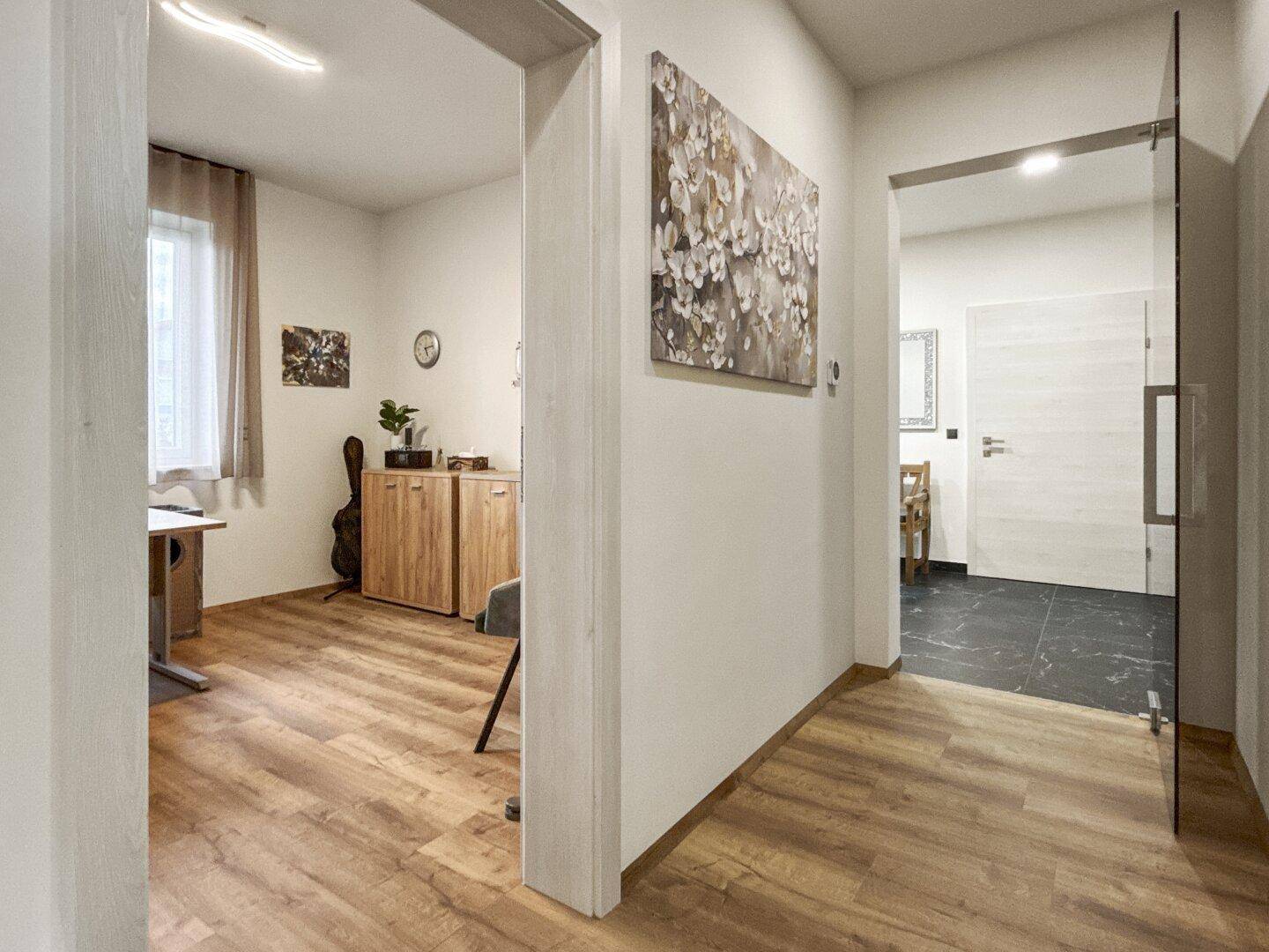 Heller Flur mit Holzboden, der zu einem Arbeitszimmer und weiteren Räumen führt.