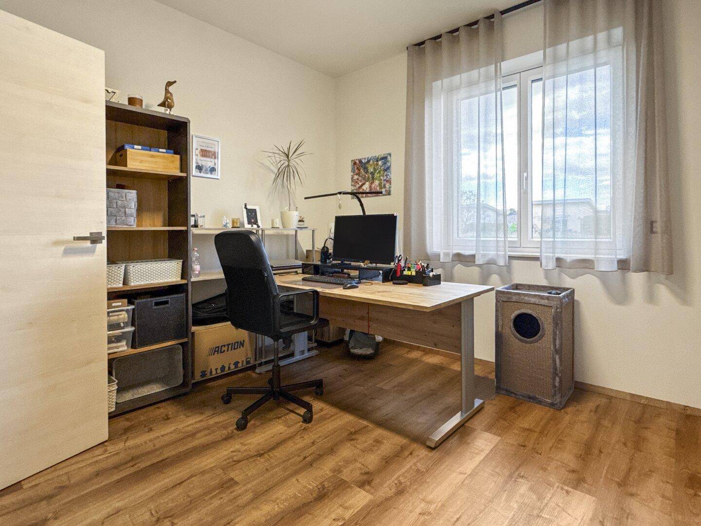 Geräumiges Arbeitszimmer mit großem Fenster, Holzboden und funktionaler Einrichtung.