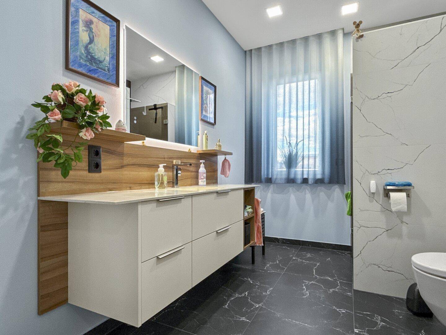 Modernes Badezimmer mit großem Waschtisch, Spiegel und dunklem Marmorboden.