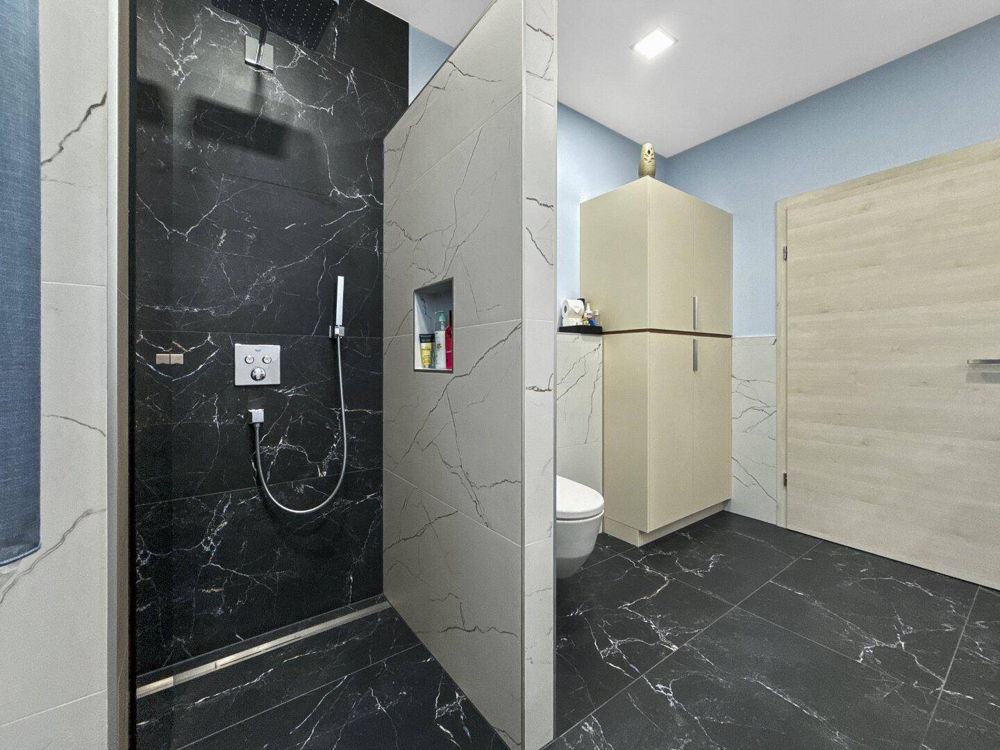 Geräumiges Badezimmer mit moderner begehbarer Dusche und dunklen Marmorfliesen am Boden.