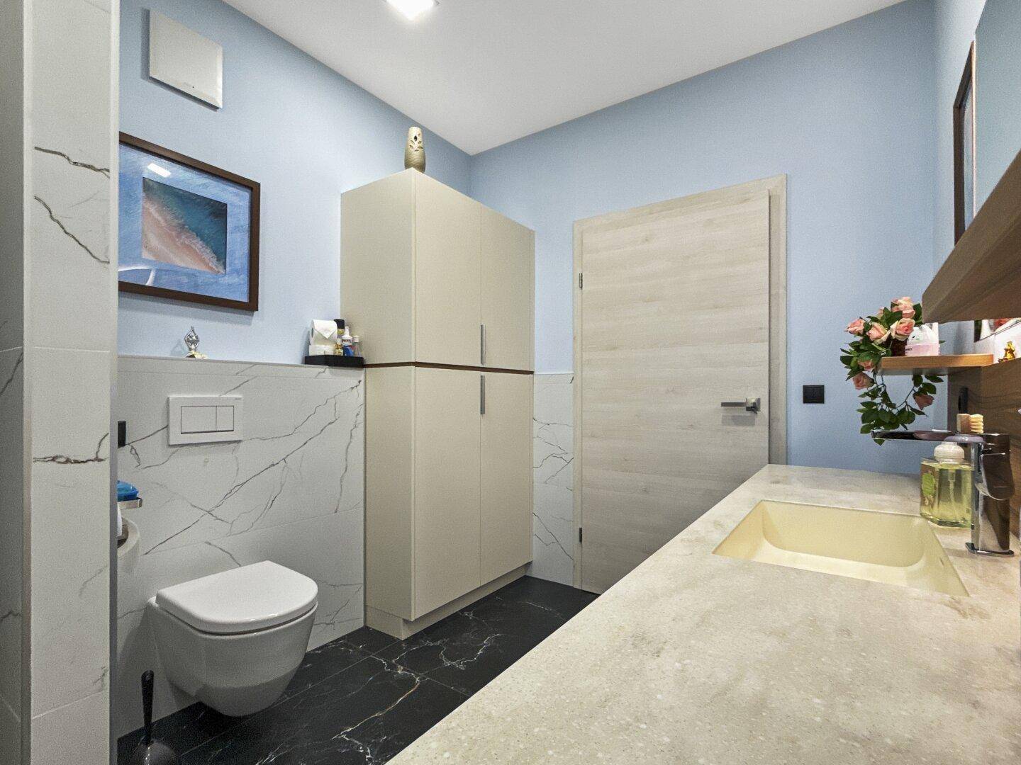 Modernes Badezimmer mit Wand-WC, Waschbecken und eleganten Marmorfliesen an den Wänden.
