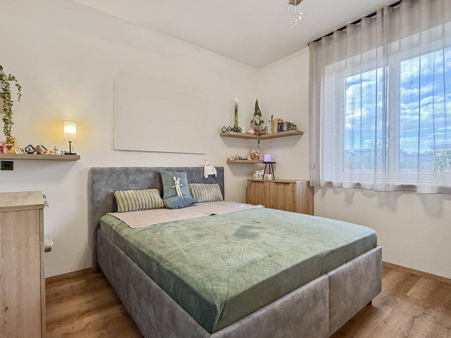 Gemütliches Schlafzimmer mit großem Fenster, Holzboden und schwebenden Wandregalen für Dekoration.