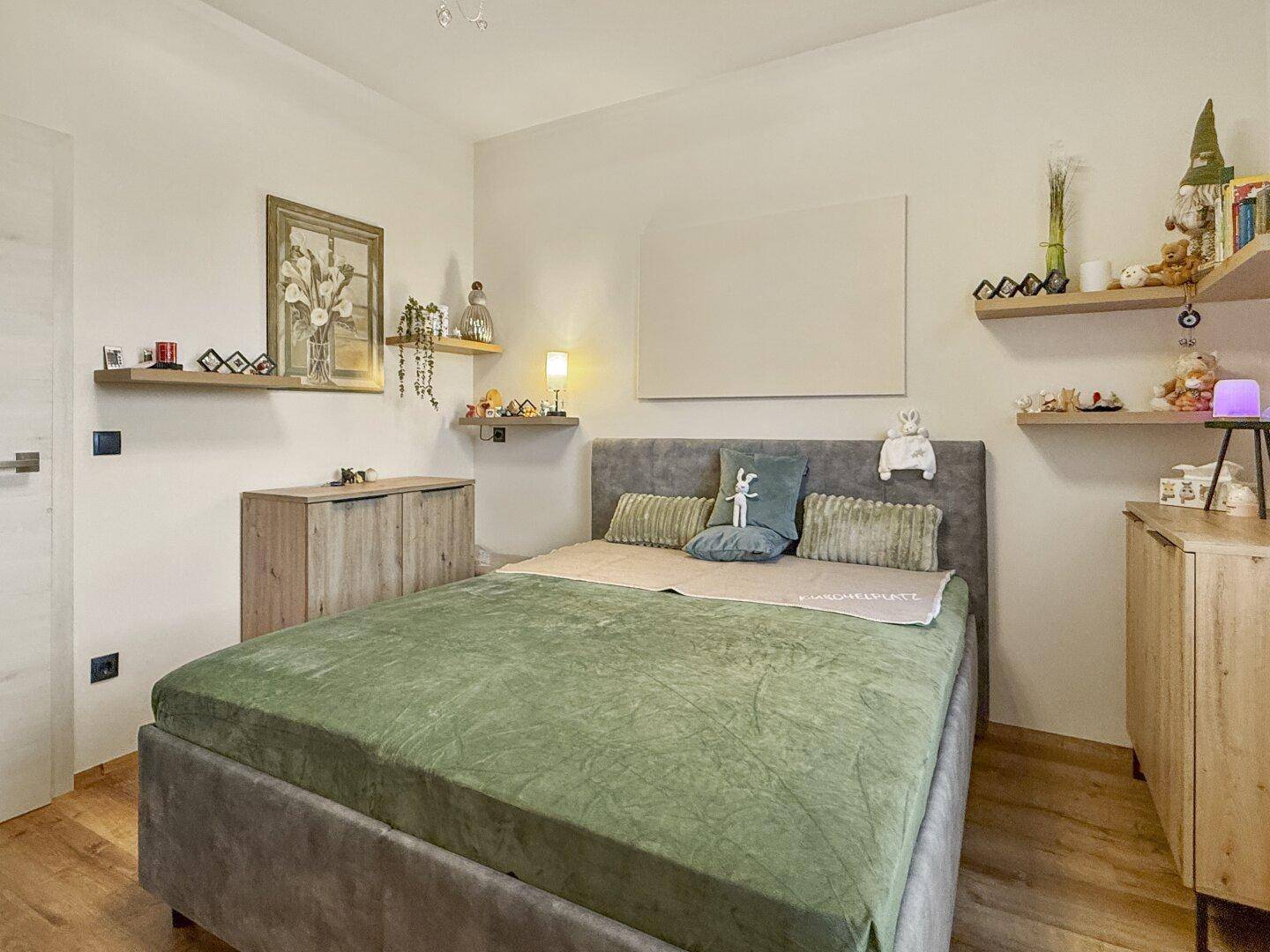 Helles Schlafzimmer mit Holzboden, bequemen Bett und dekorativen Wandregalen für persönliche Gegenstände.