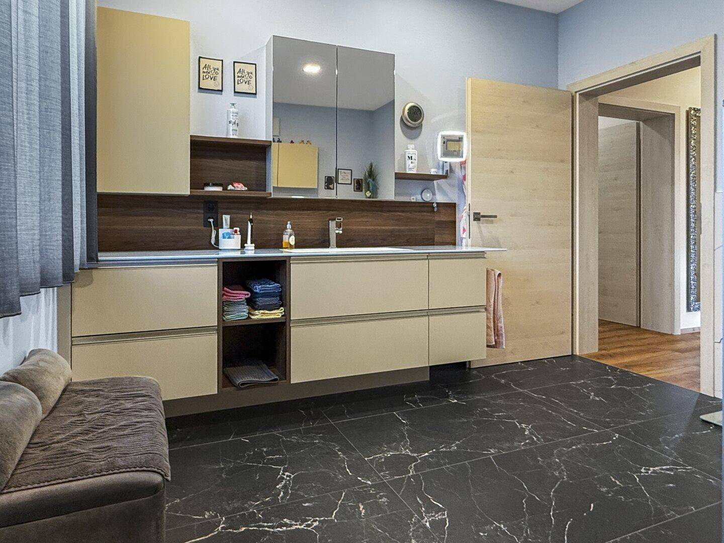 Modernes Badezimmer mit Doppelwaschbecken, Spiegelschrank und dunklen Fliesen am Boden.