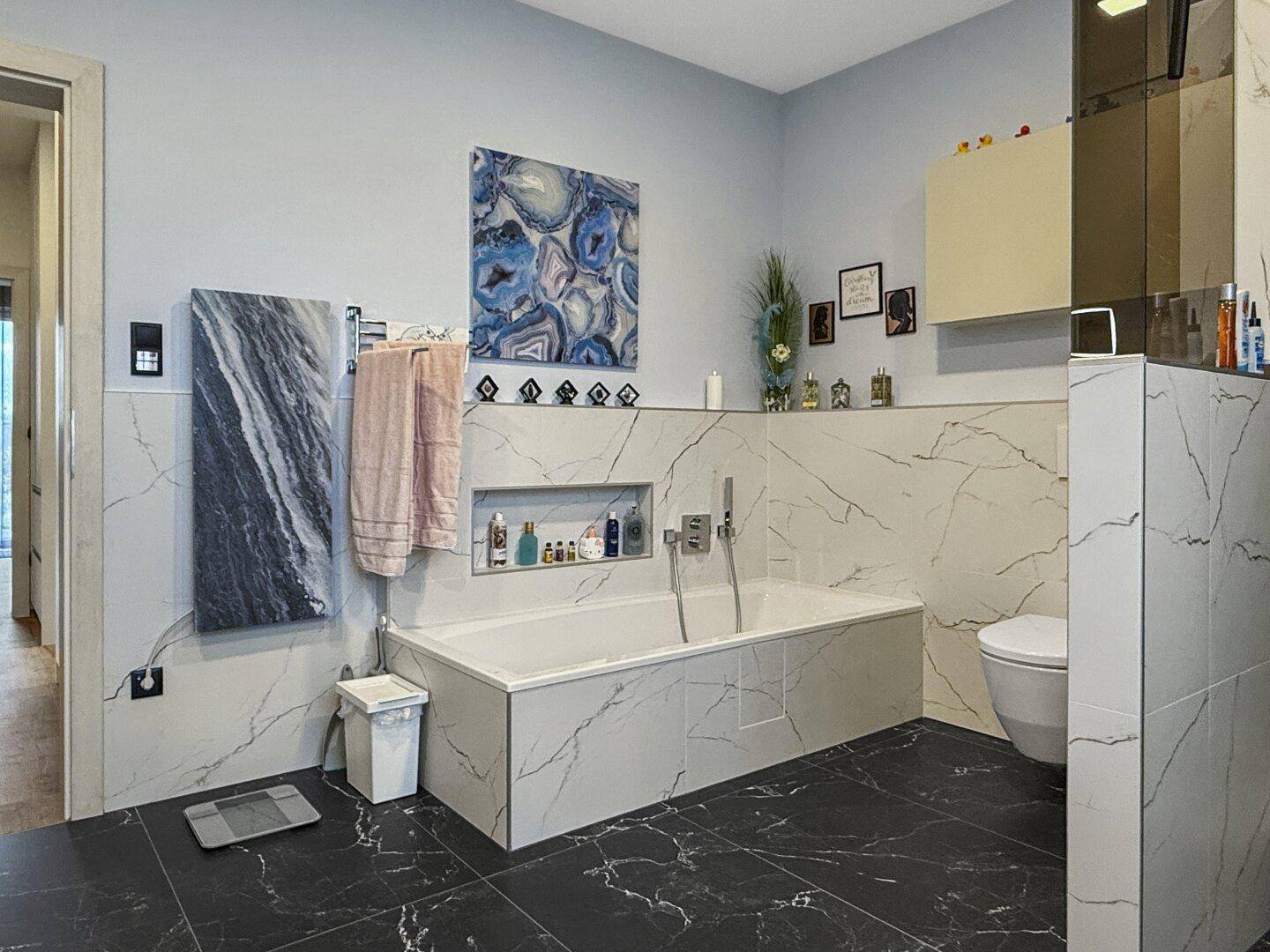 Elegantes Badezimmer mit Badewanne, Wand-WC und stilvollen Marmorfliesen an Wänden und Boden.