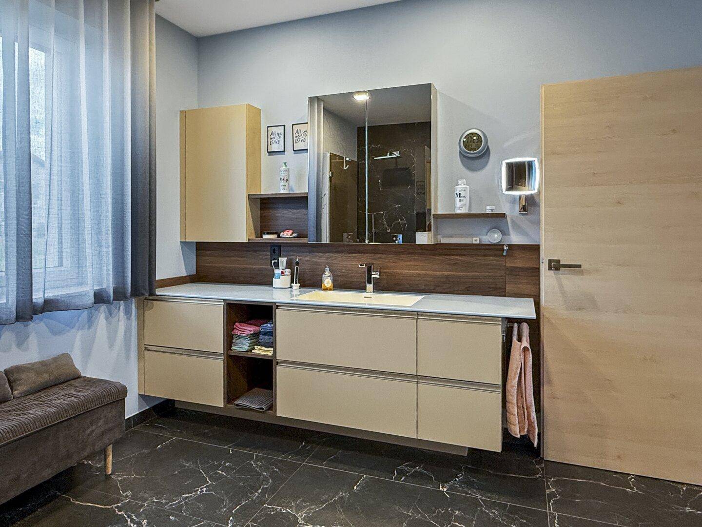 Helles Badezimmer mit Doppelwaschbecken, Spiegelschrank und großem Fenster für Tageslicht.