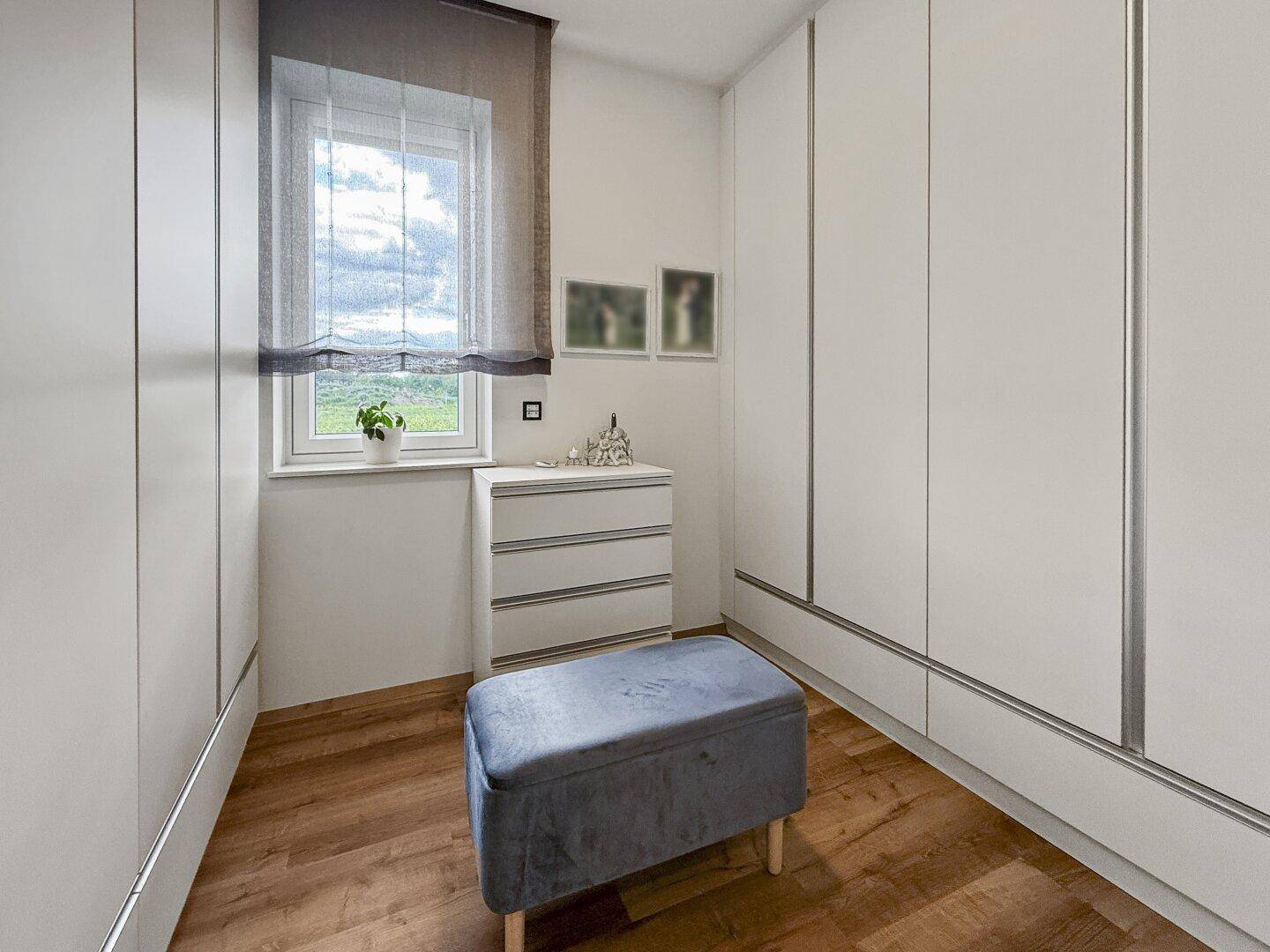 Begehbarer Kleiderschrank mit Einbauschränken, Fenster und einer bequemen Sitzgelegenheit.