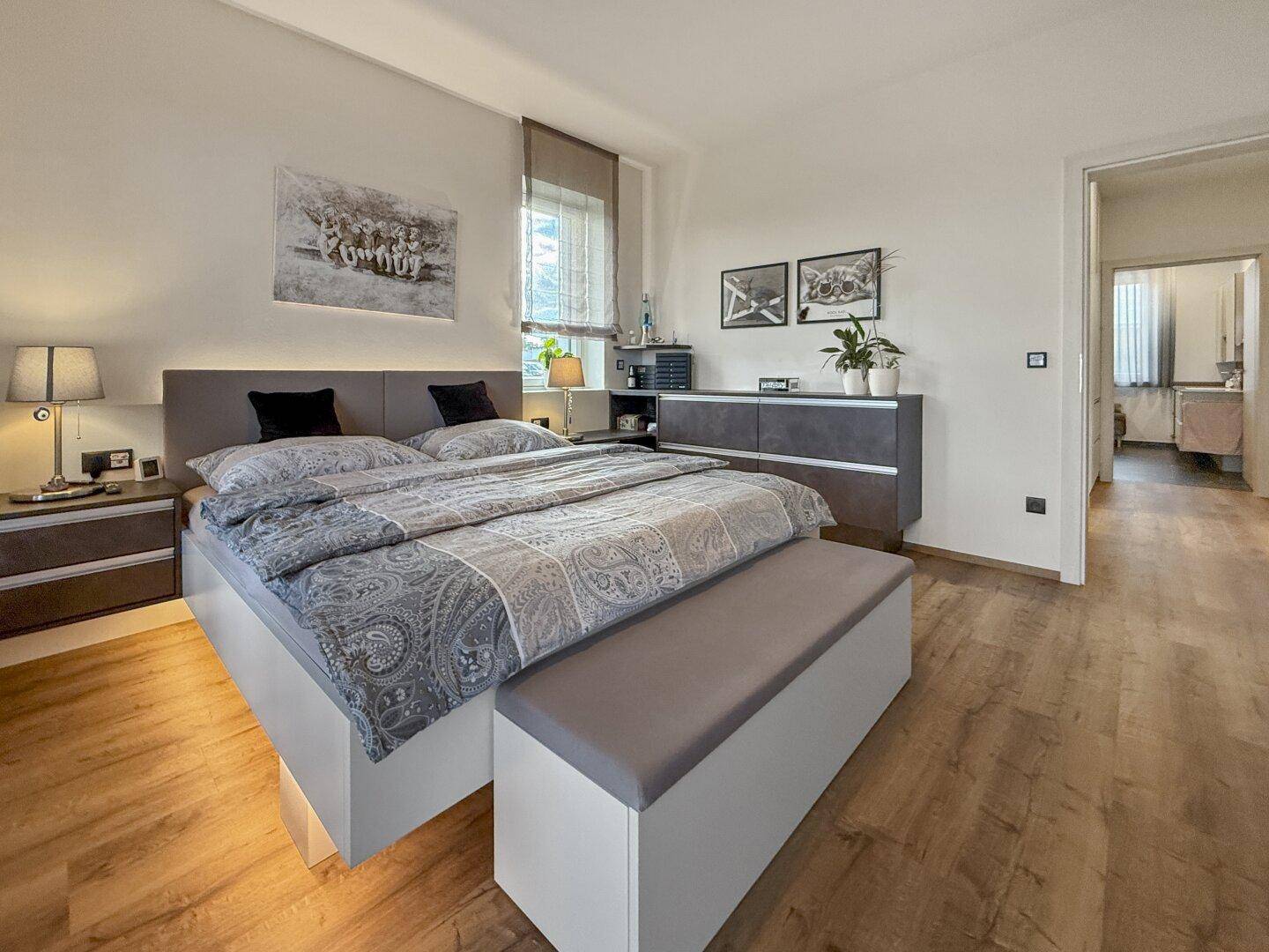 Geräumiges Schlafzimmer mit Doppelbett, Holzboden und modernen Nachttischen mit Beleuchtung.