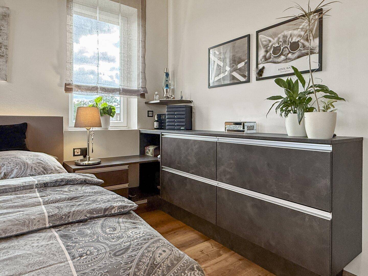 Schlafzimmer mit Holzboden, Fenster und modernen Möbeln, die viel Stauraum bieten.