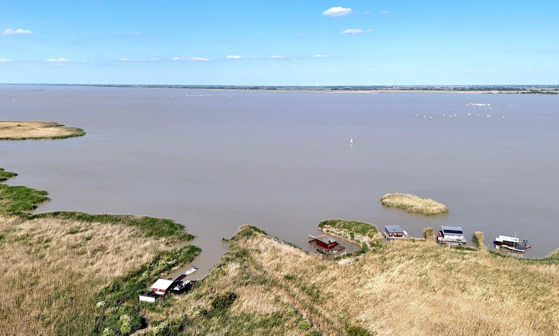Panoramablick über die weite Seenlandschaft mit Schilfinseln und kleinen Gebäuden.