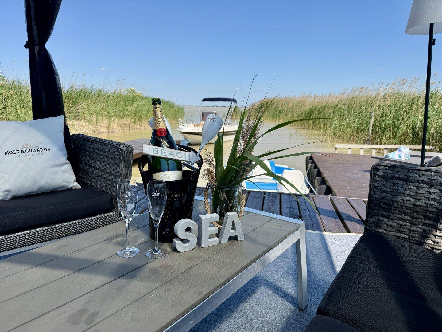 Gemütlicher Sitzbereich im Pavillon mit Champagner und Blick auf das Wasser und Schilf.