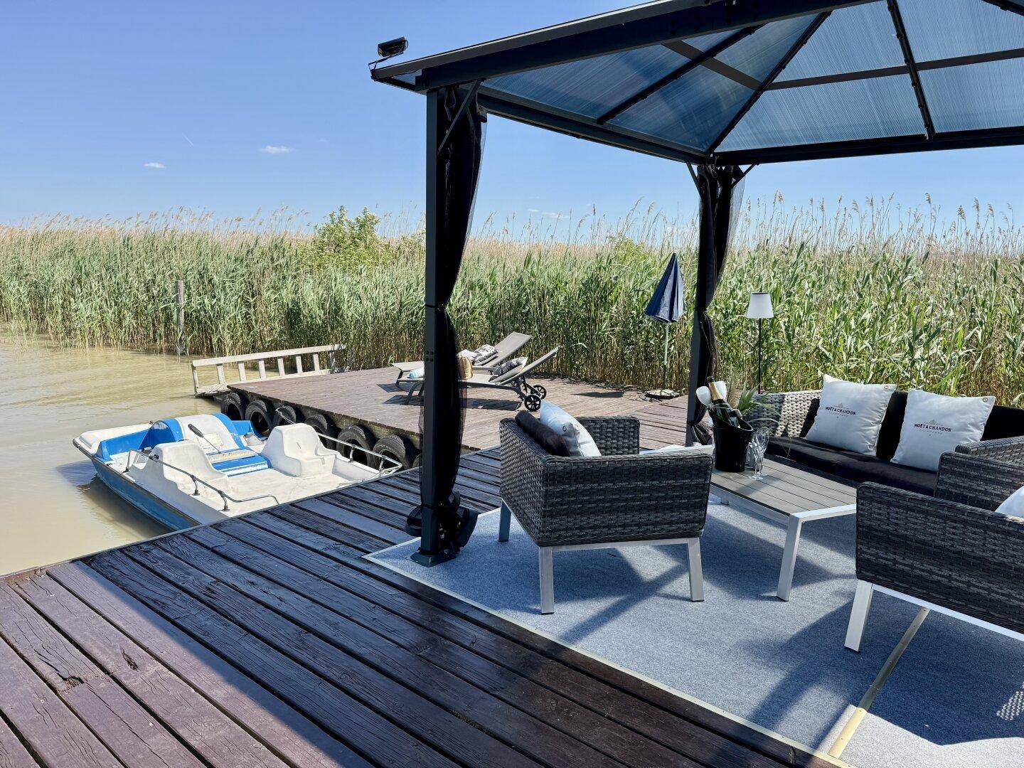 Weitläufiger Holzsteg mit Tretboot und einem einladenden Pavillon mit Lounge-Möbeln.