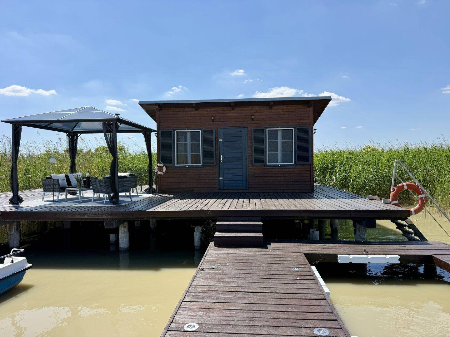 Vorderansicht des Holzhauses auf dem Steg mit Fensterläden und einem möblierten Pavillon.