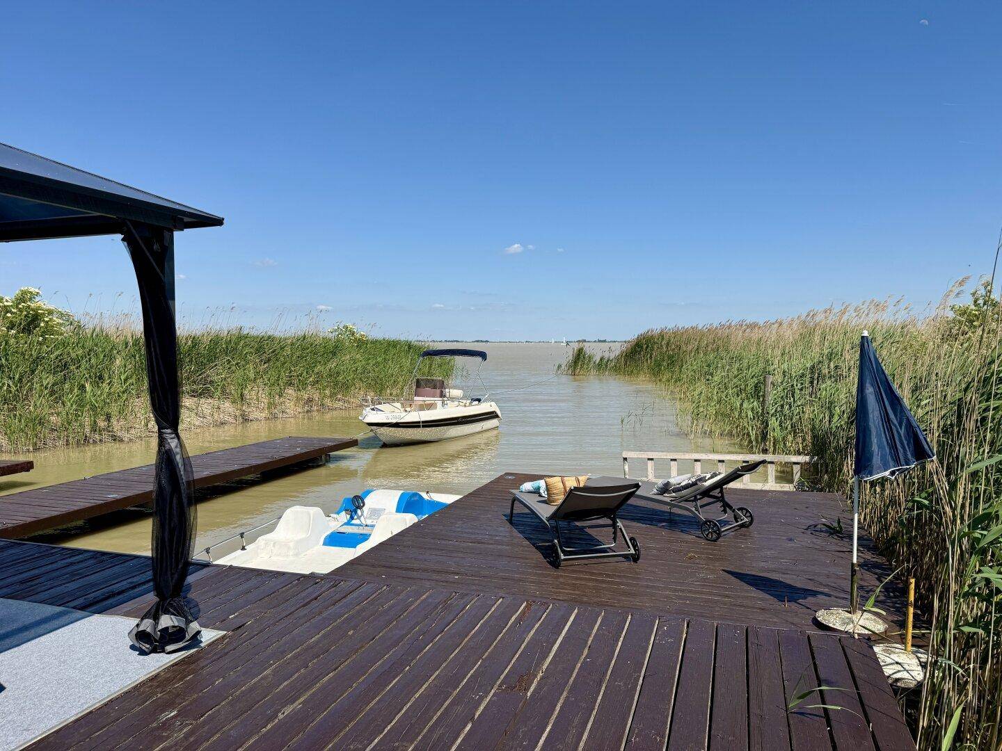 Sonniger Steg mit Liegestühlen und Blick auf das offene Wasser mit einem Motorboot.