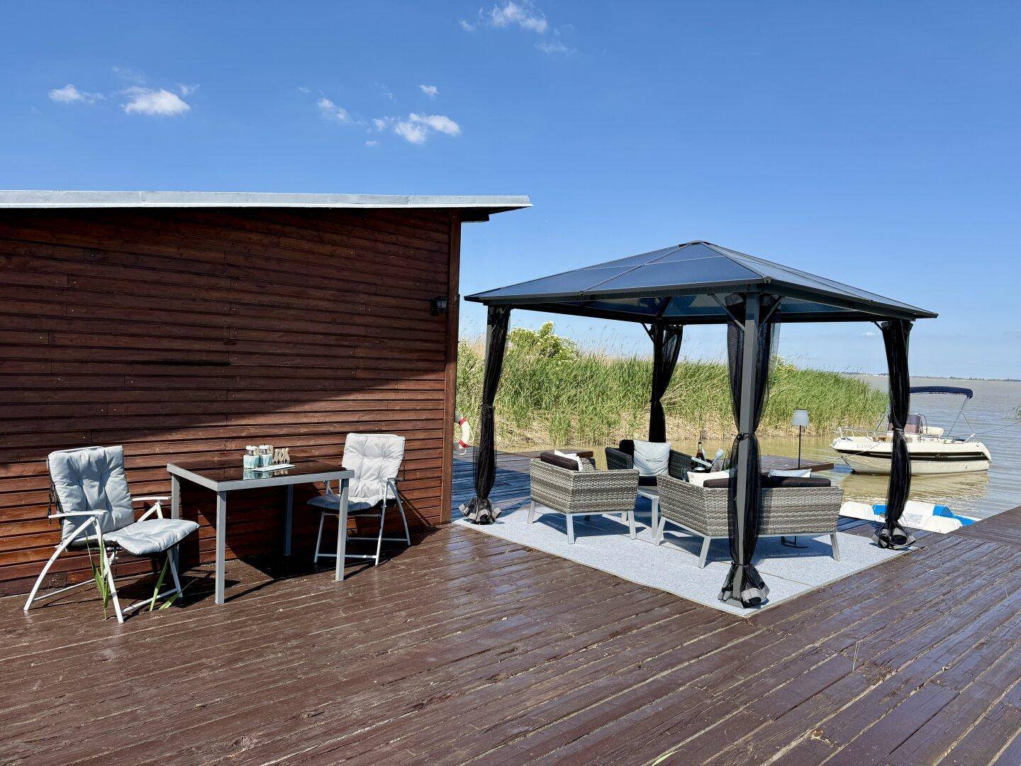 Holzhaus mit kleinem Essbereich im Freien und einem Pavillon mit Lounge-Möbeln auf dem Steg.