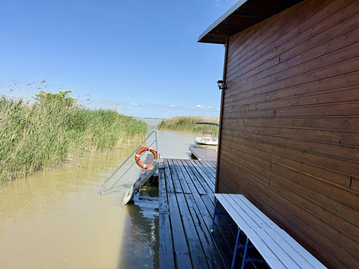 Seitenansicht des Holzhauses auf dem Steg mit Rettungsring und Zugang zum Wasser.