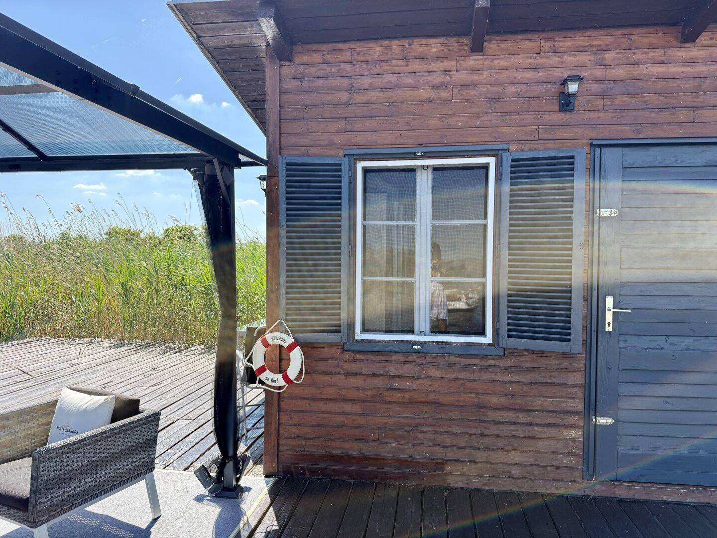 Detailansicht des Holzhauses mit Fenster, Fensterläden und einem Rettungsring an der Wand.