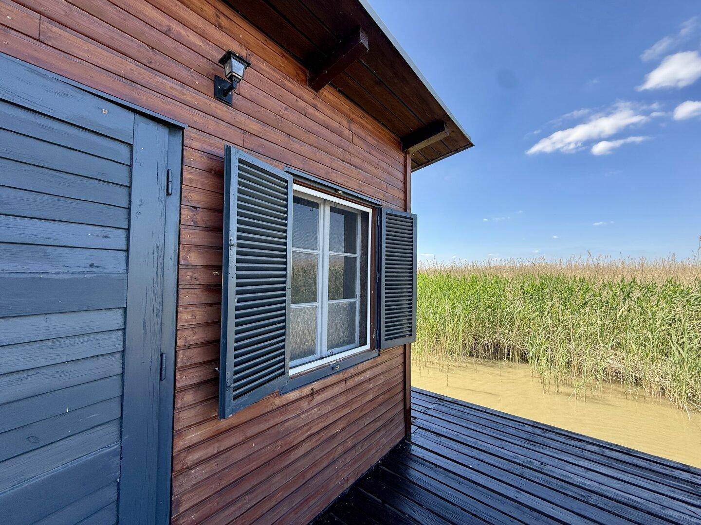 Fenster und Tür des Holzhauses mit Blick auf den Holzsteg und das ruhige Wasser.