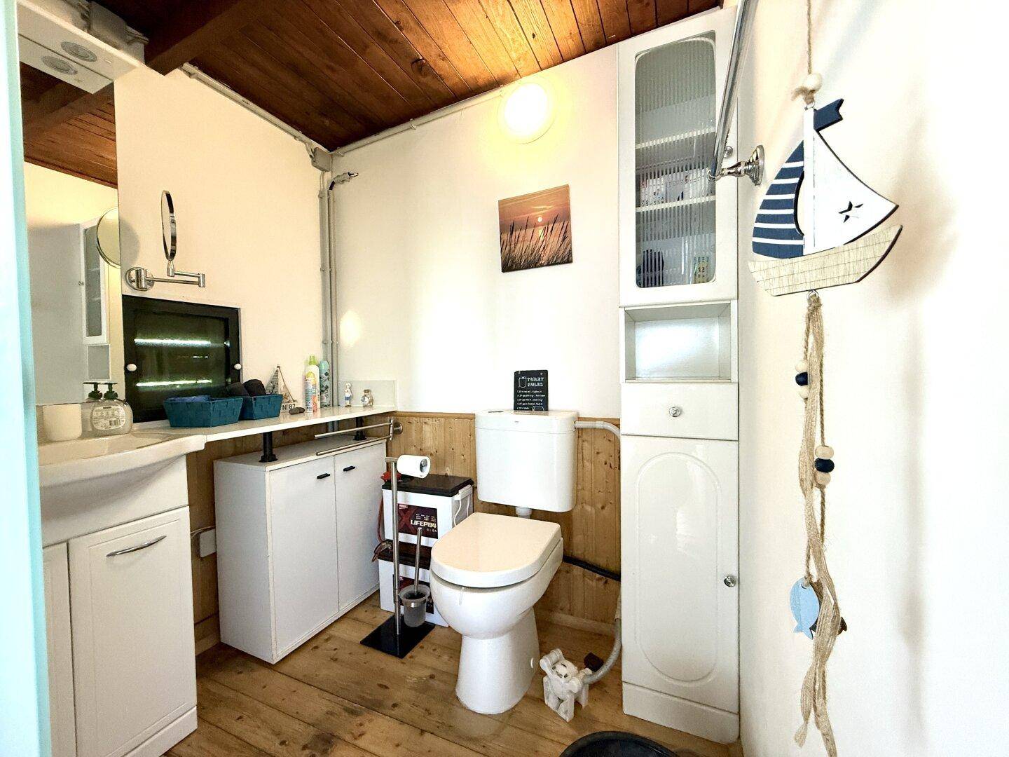 Kleines WC mit Waschbecken, Toilette und maritimer Dekoration, funktional eingerichtet.
