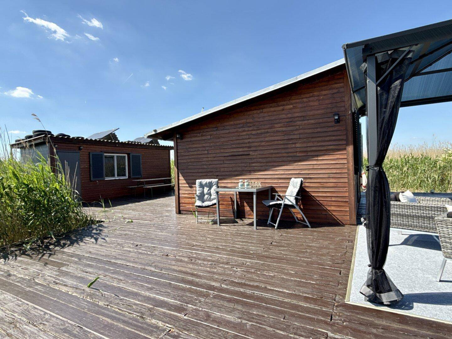 Große Holzterrasse mit Sitzgelegenheiten und einem Pavillon, umgeben von Schilf und Natur.