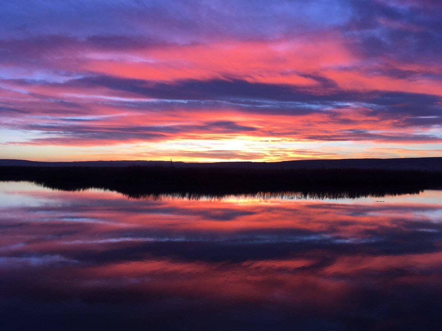 Spektakulärer Sonnenuntergang über dem See mit leuchtenden Farben und Spiegelungen im Wasser.