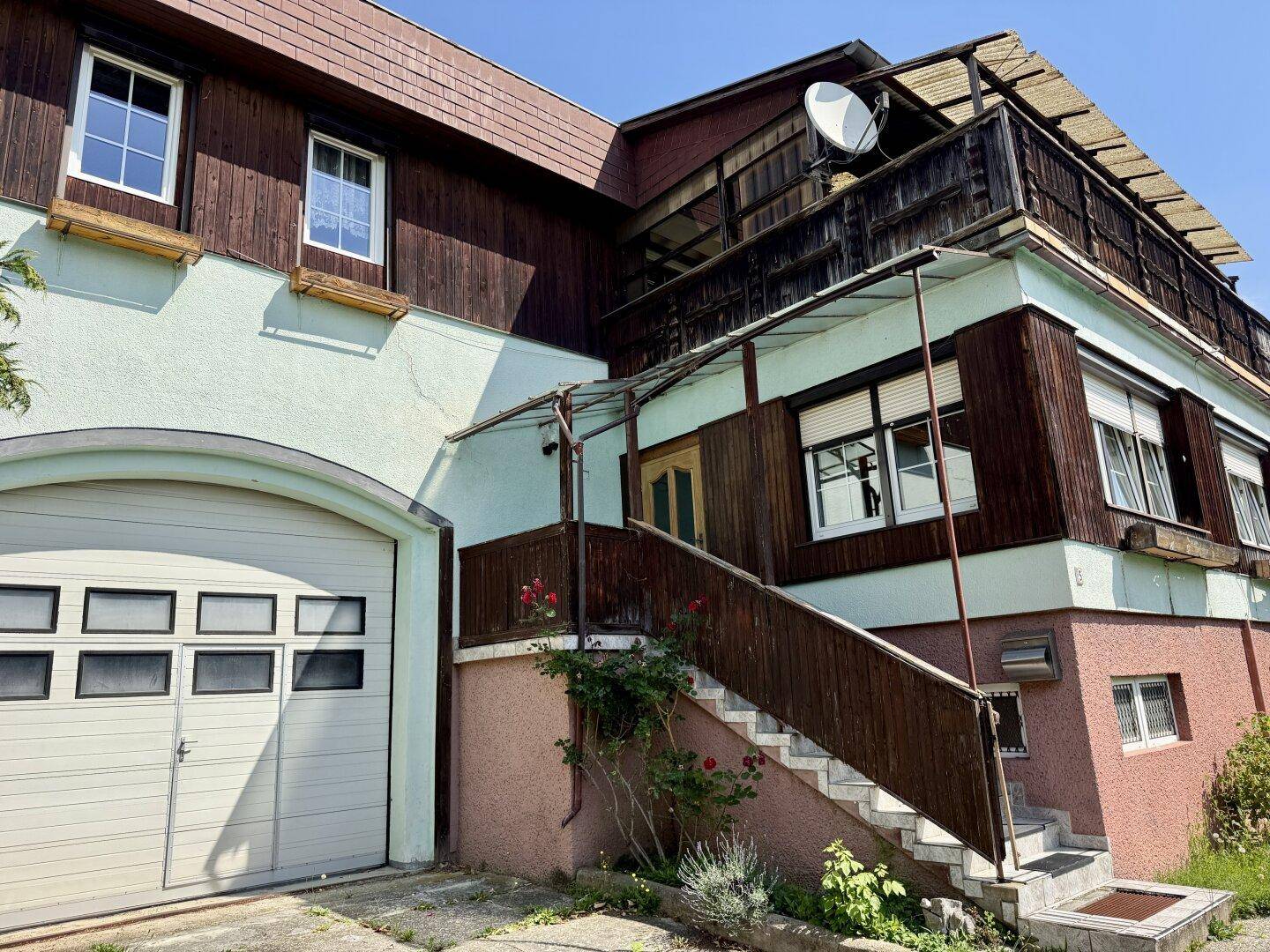 Außenansicht eines Hauses mit Garage, Außentreppe und einer Kombination aus Holz- und Putzfassade.