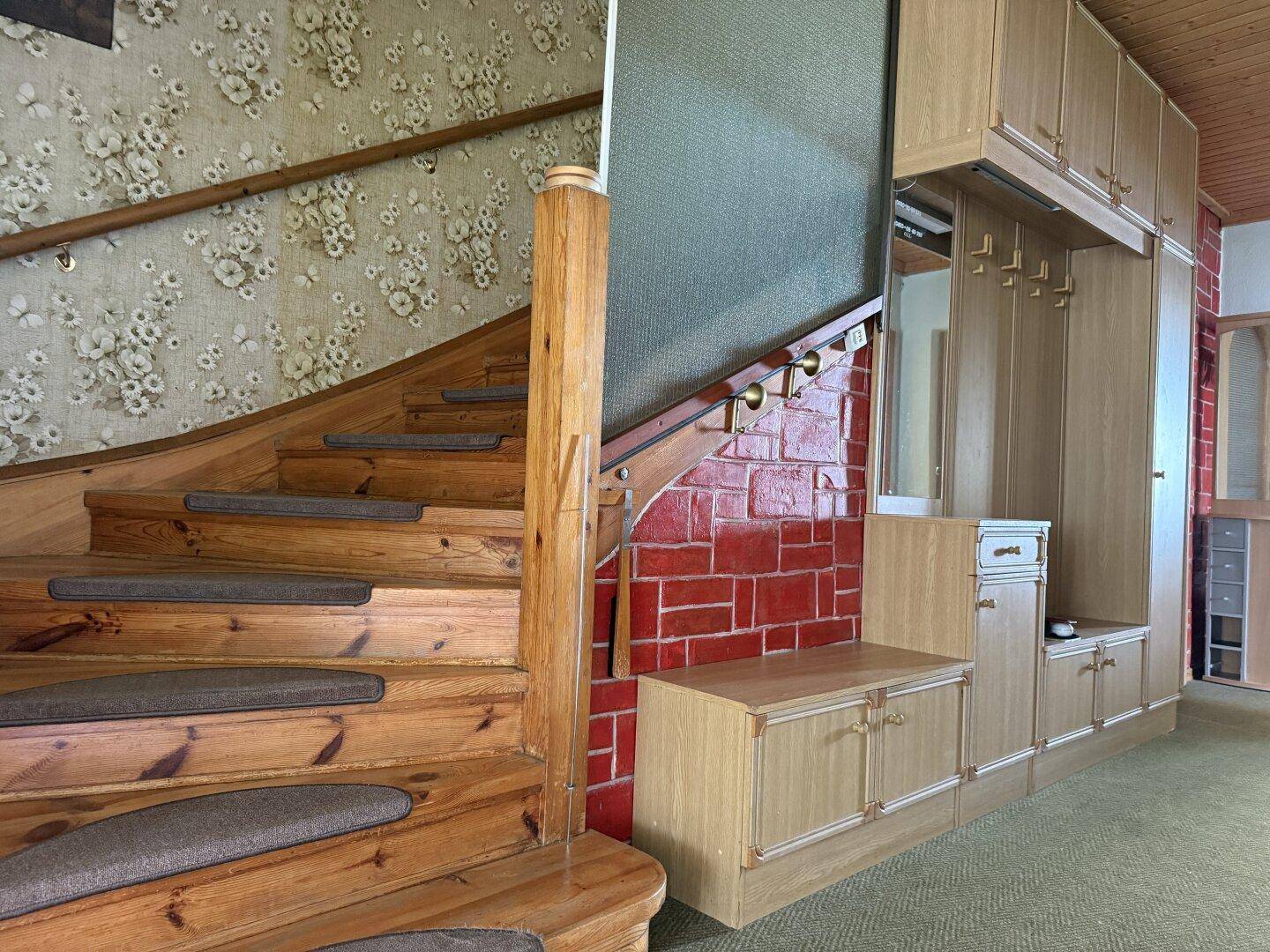 Holztreppe mit Teppichstufen und floraler Tapete im Flur.