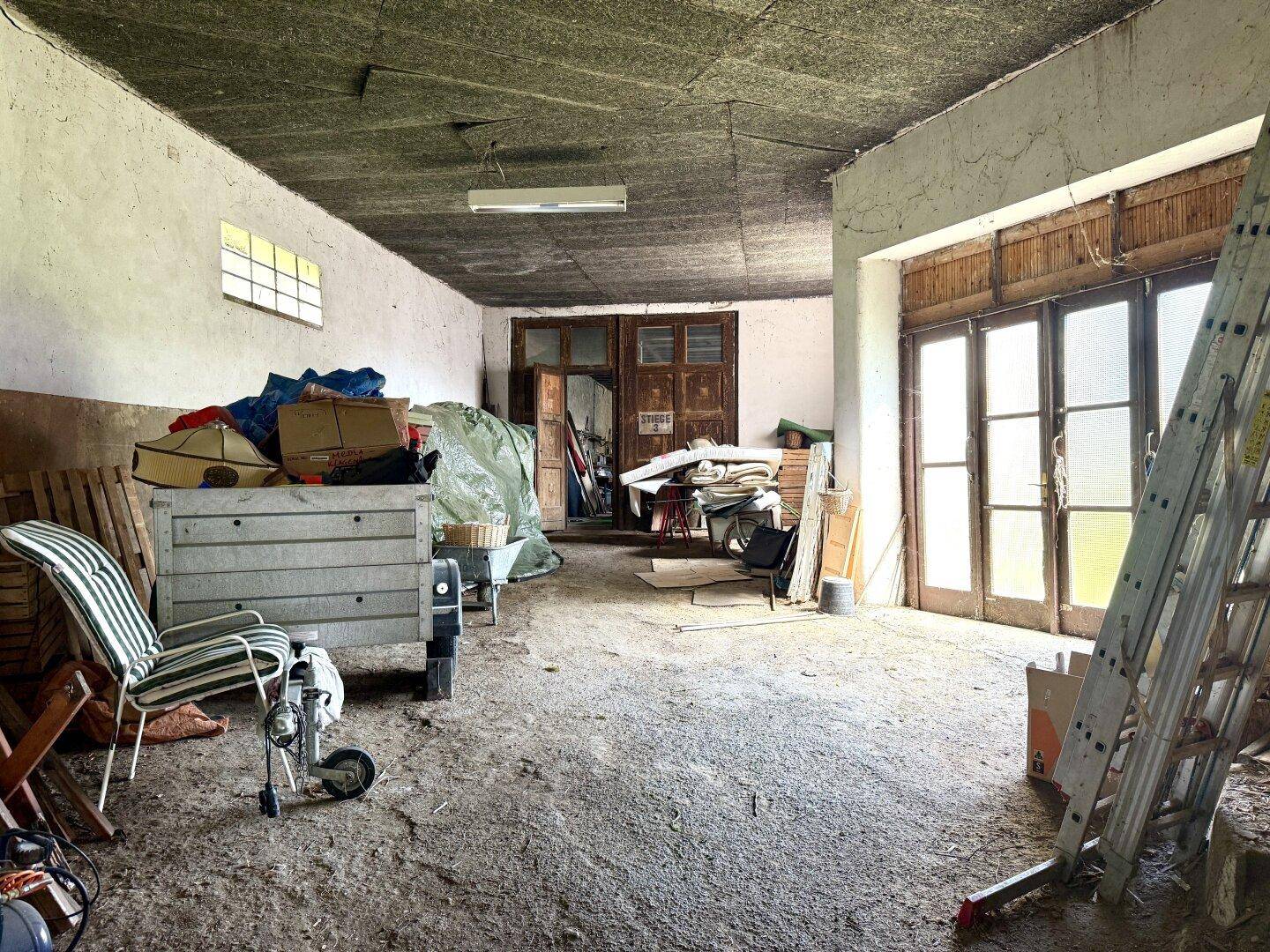 Großer Lagerraum mit Betonboden, alten Holztüren und einer Vielzahl von gelagerten Gegenständen.