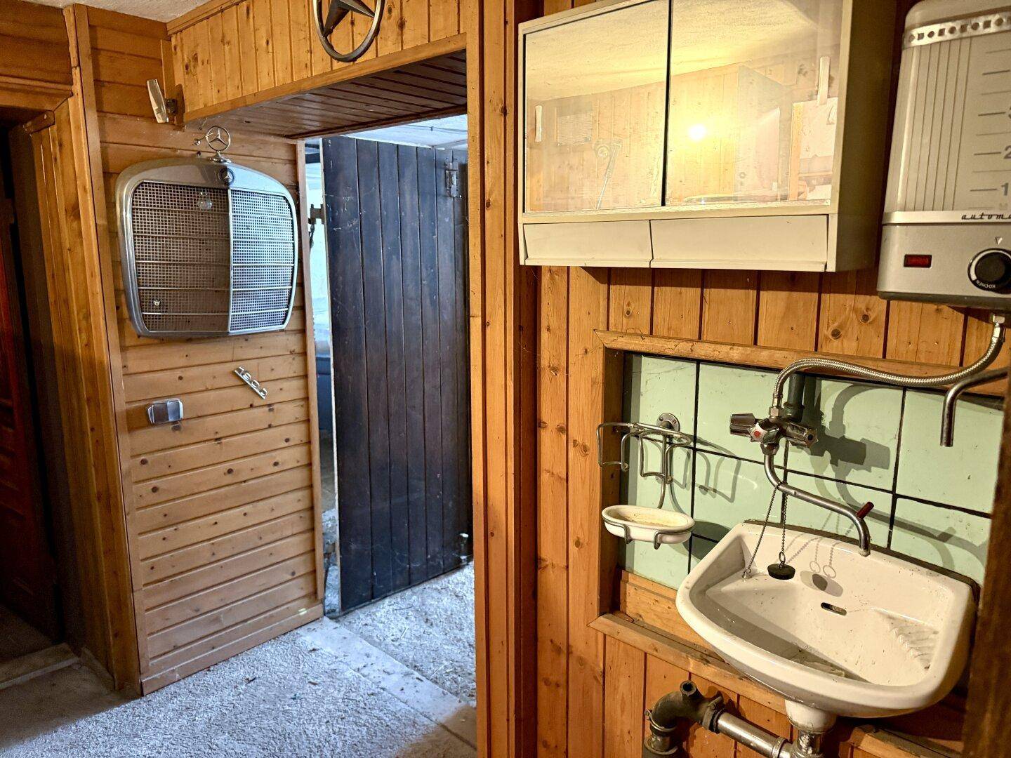 Rustikaler Waschraum mit Holzverkleidung, kleinem Waschbecken, Spiegelschrank und einem alten Heizkörper.