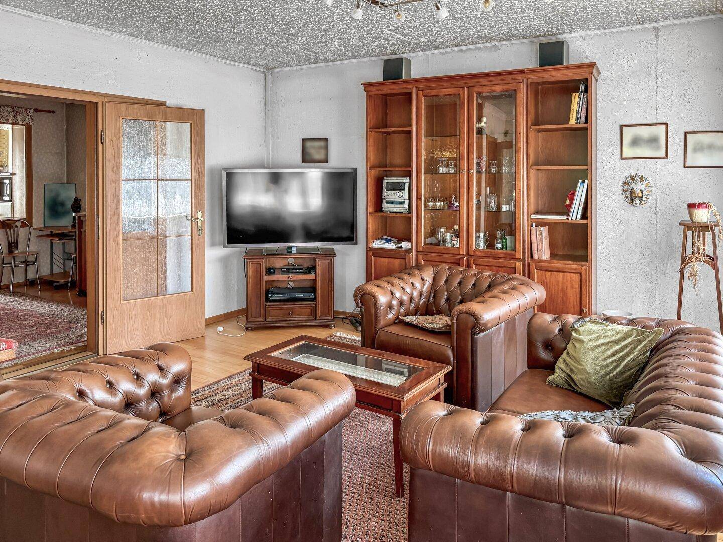 Traditionelles Wohnzimmer mit Ledermöbeln, Vitrinenschrank und Fernseher.