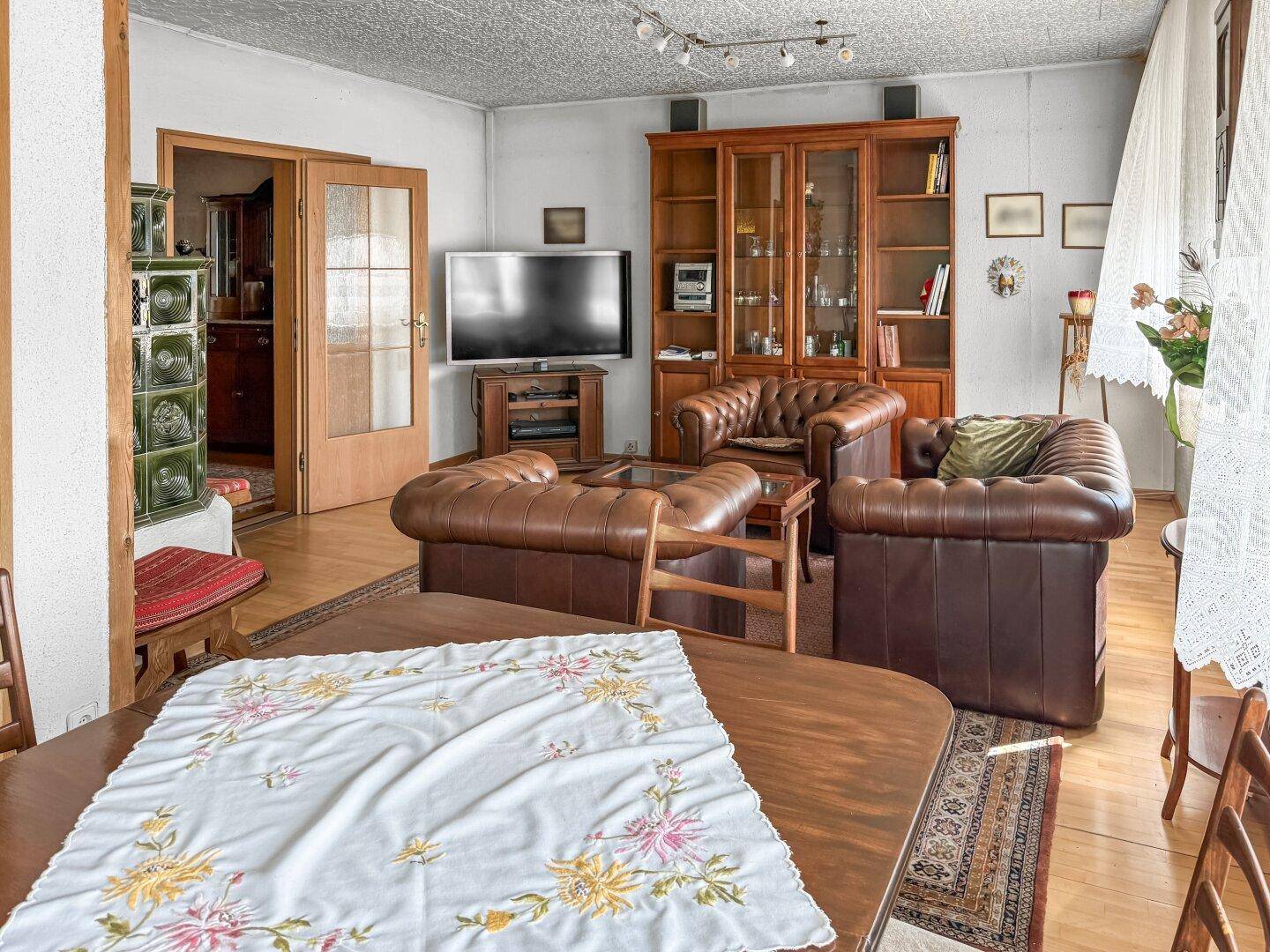 Geräumiges Wohnzimmer mit traditionellen Ledersofas, Holzboden und einem Kachelofen im Hintergrund.