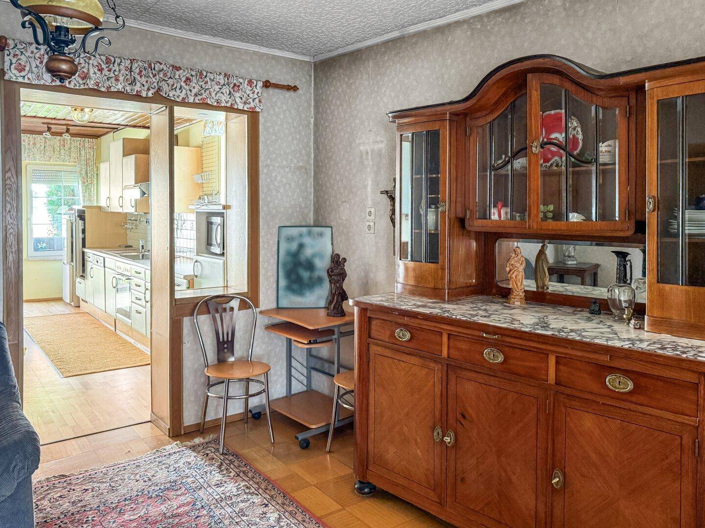 Wohnbereich mit traditionellem Holzschrank und Blick in die angrenzende Küche.