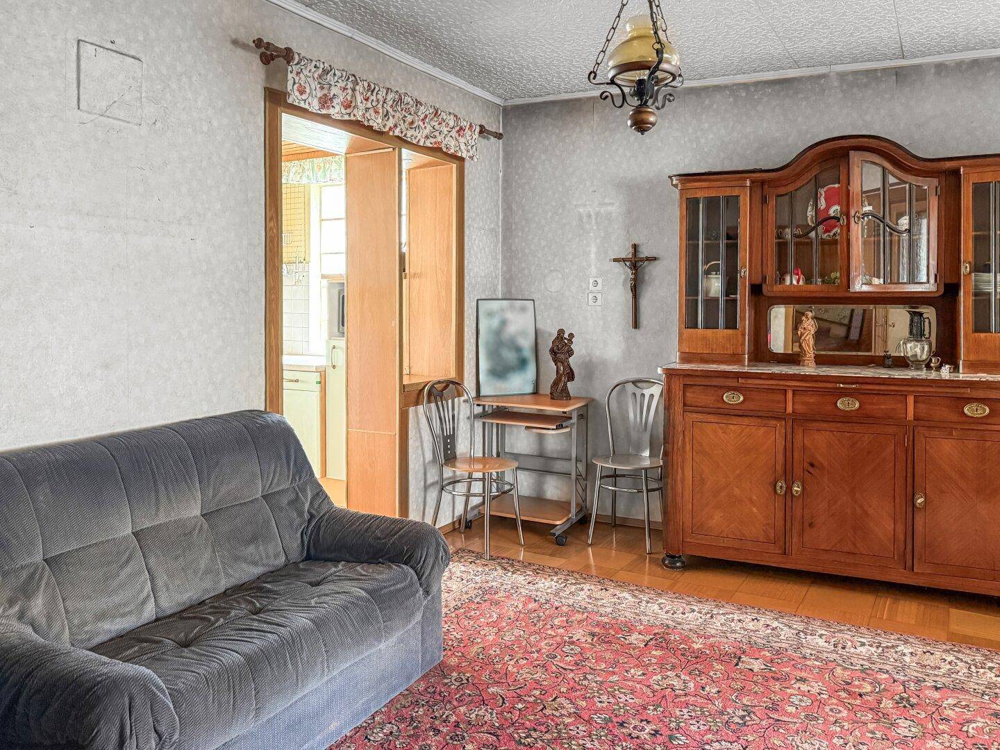Gemütliches Wohnzimmer mit einem Sofa, einem antiken Holzschrank und einem Teppichboden.