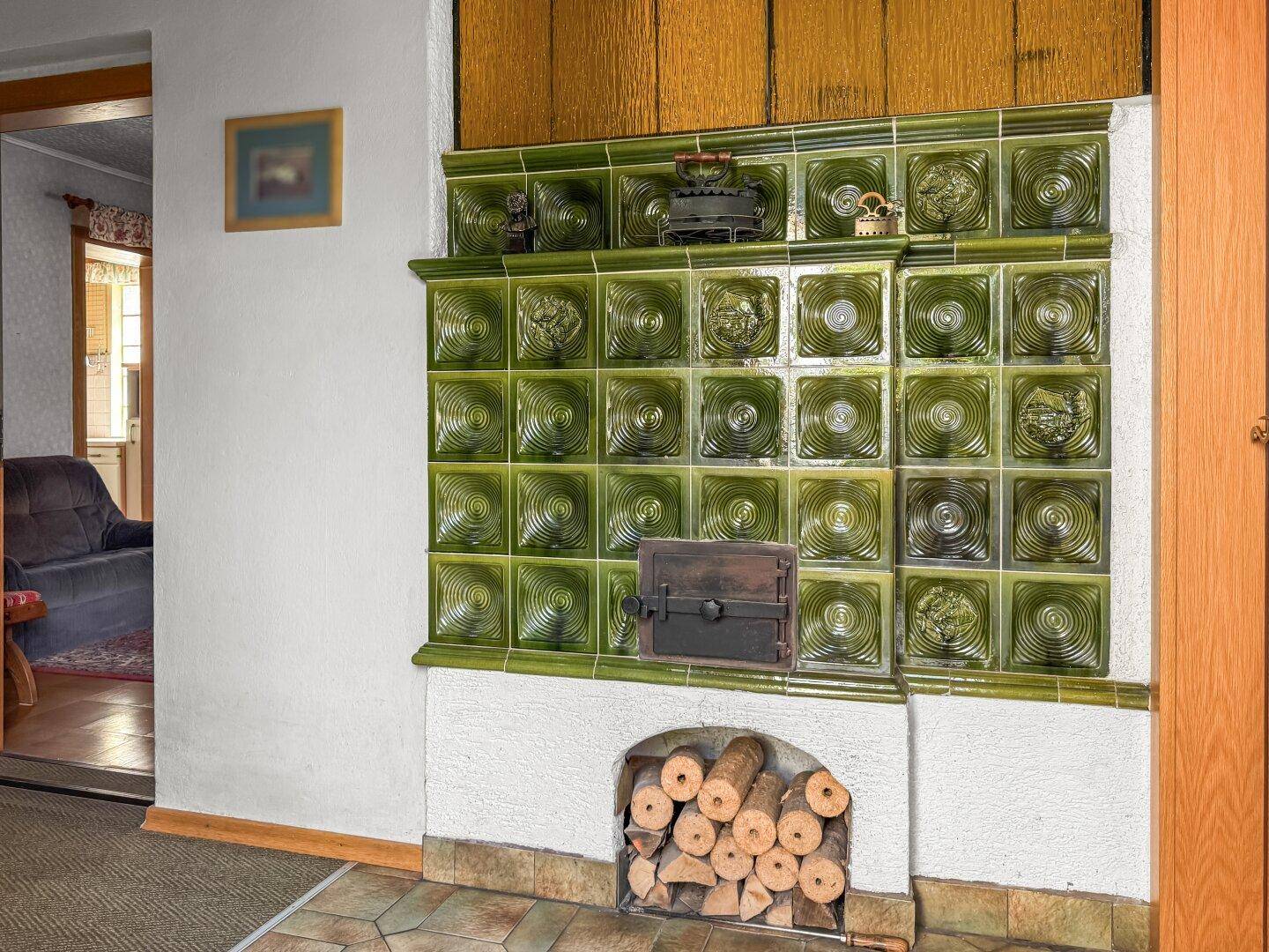 Detailansicht eines traditionellen grünen Kachelofens mit Holzscheiten im unteren Fach.