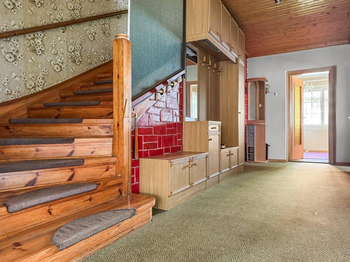 Geräumiger Flur mit Holztreppe, Garderobe und Teppichboden.