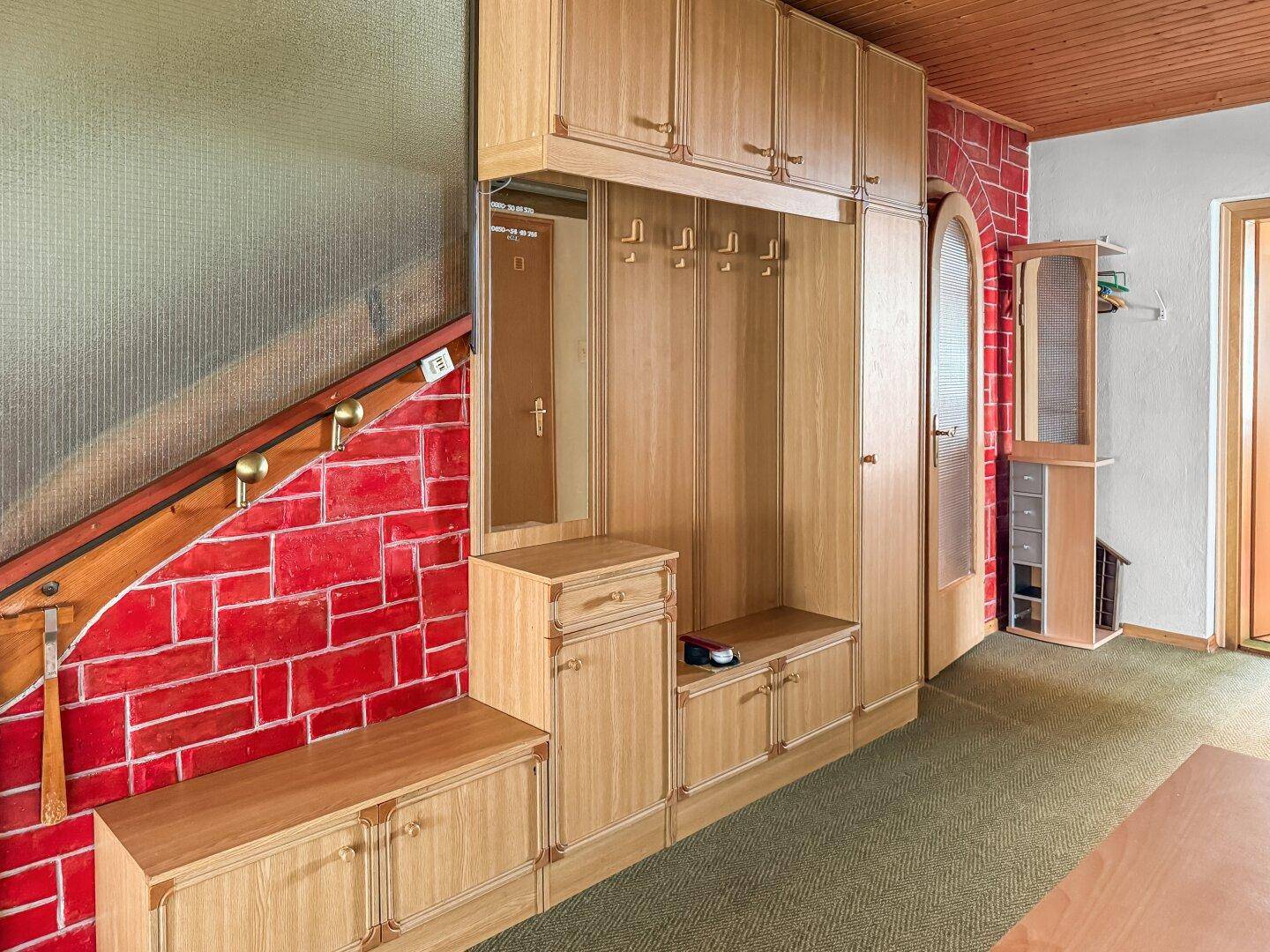 Eingangsbereich mit Garderobe aus hellem Holz und roter Ziegelwandverkleidung.