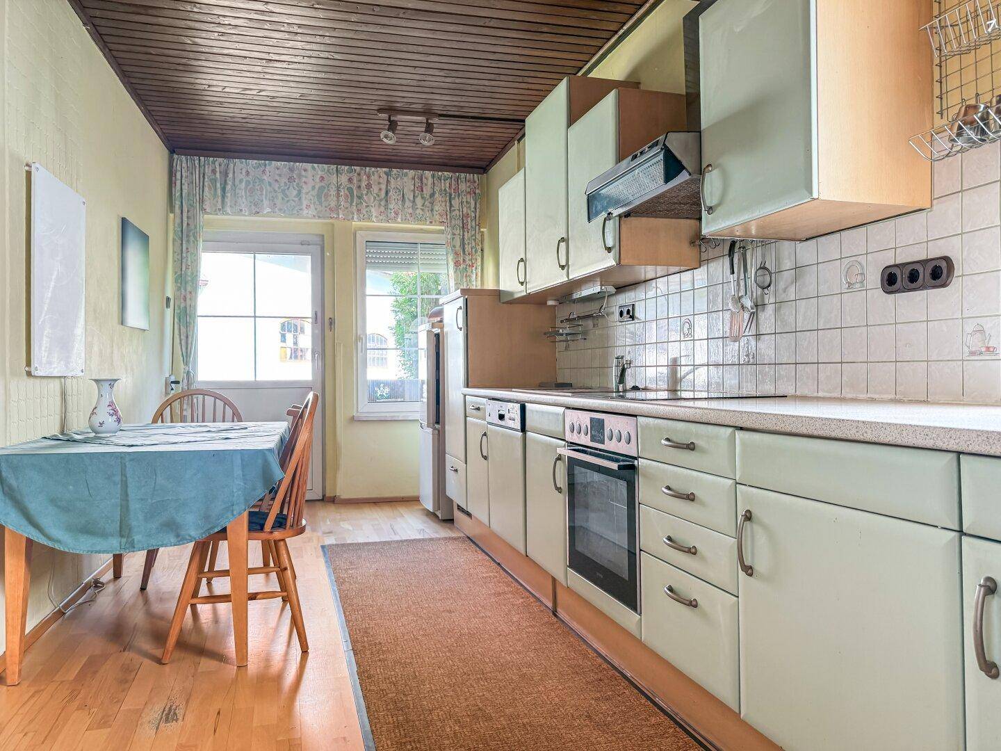 Helle Küche mit Esstisch, hellgrünen Schränken und Holzbalkendecke.