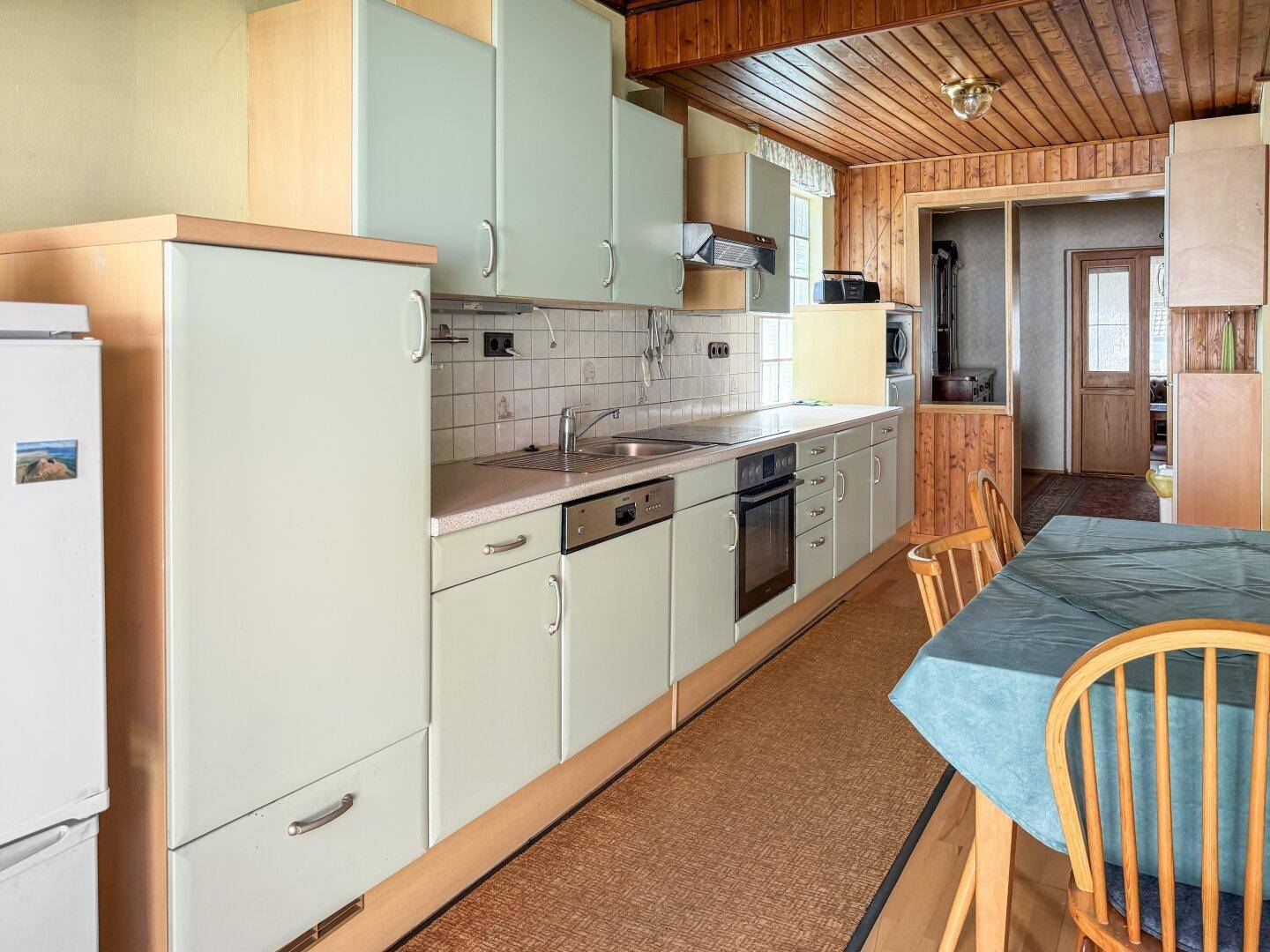 Funktionale Küche mit hellgrünen Fronten, Holzbalkendecke und Essbereich.