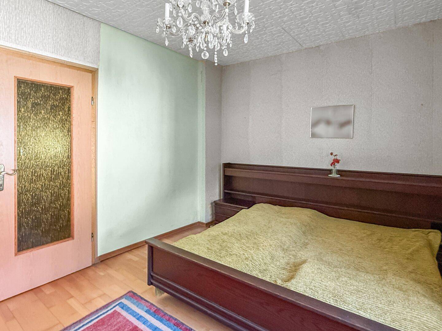 Schlafzimmer mit Doppelbett, Holzboden und einem Kronleuchter an der Decke.