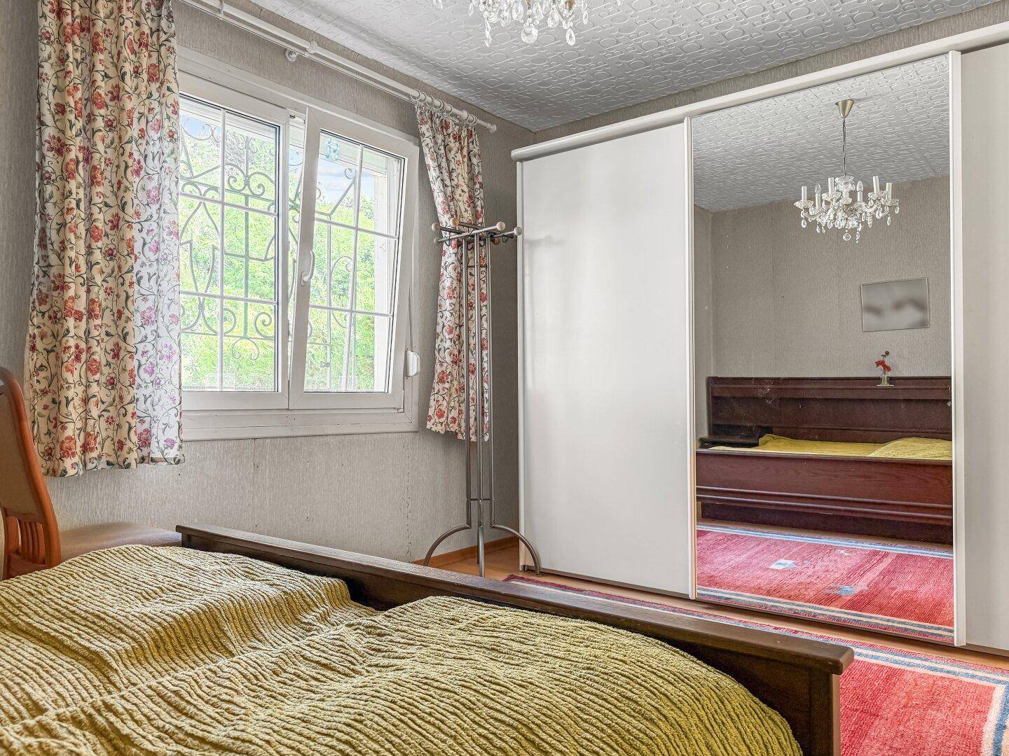 Schlafzimmer mit Doppelbett, Spiegelschrank und Fenster mit Blick ins Grüne.