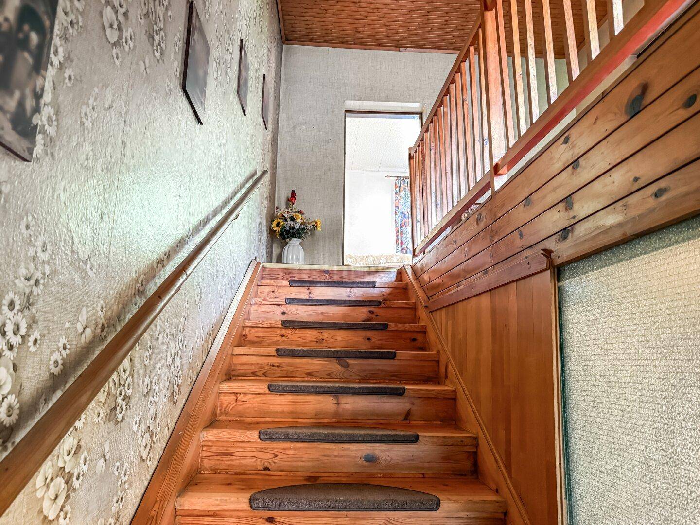 Holztreppe mit Geländer und floraler Tapete, die in das obere Stockwerk führt.