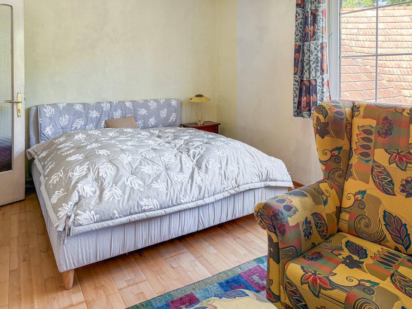 Schlafzimmer mit Doppelbett, Holzboden und einem bunten Sessel.