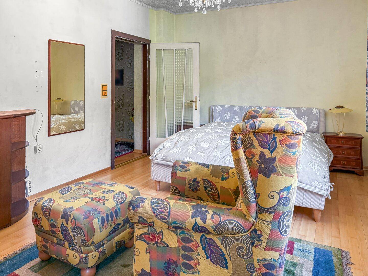 Schlafzimmer mit Doppelbett, Sessel und Spiegel an der Wand.