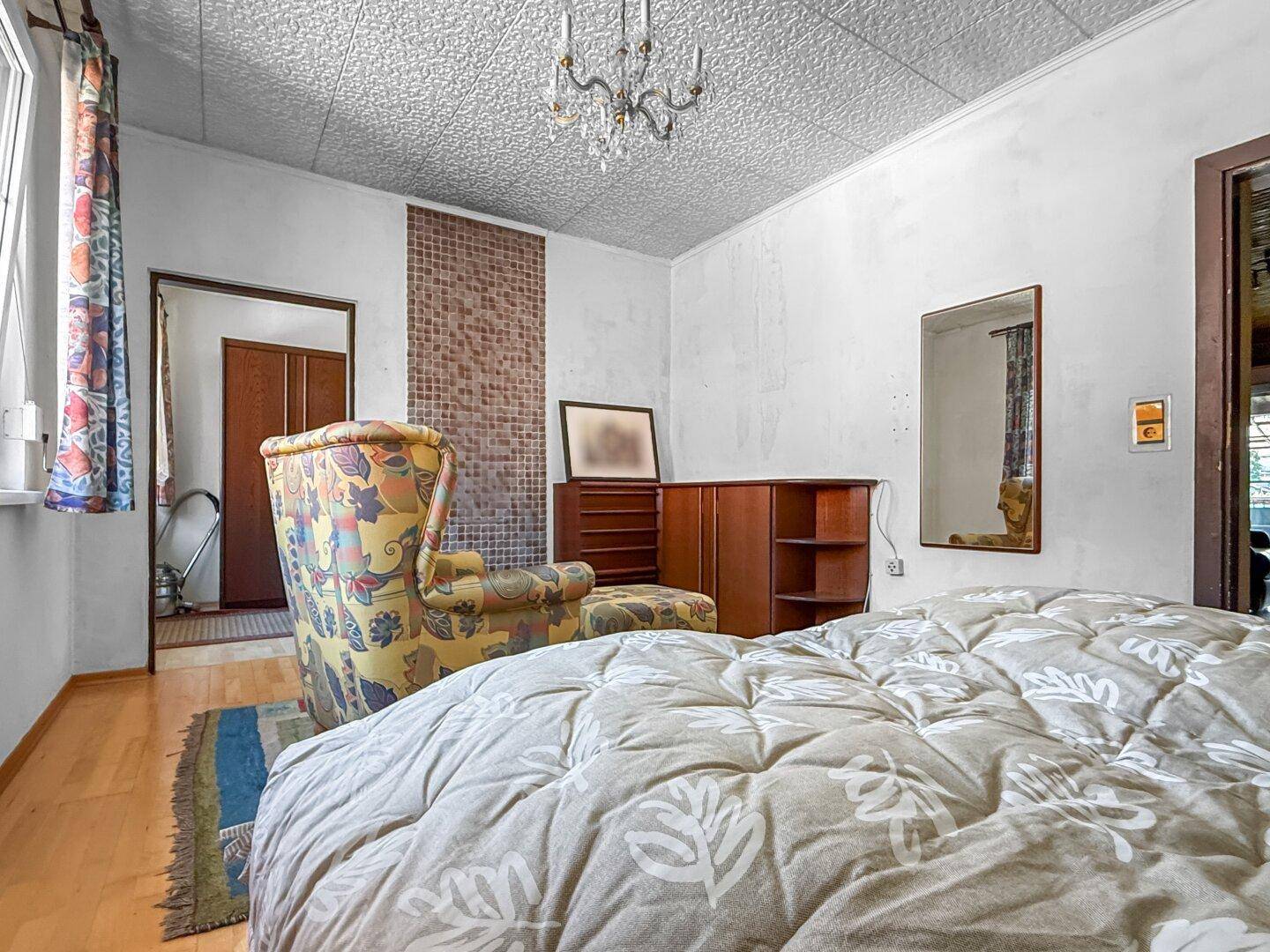 Schlafzimmer mit Doppelbett, Sessel und Blick auf den Flur.