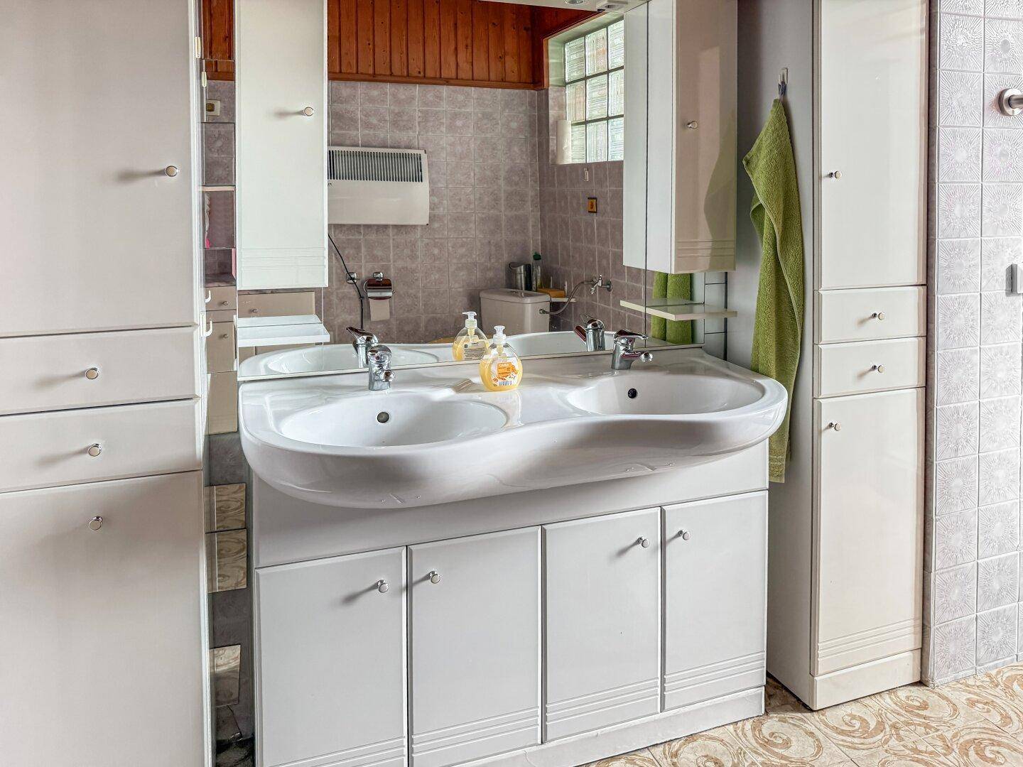 Badezimmer mit Doppelwaschbecken, Spiegelschrank und Heizkörper.