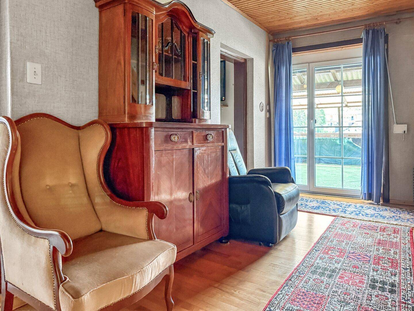 Wohnbereich mit traditionellem Holzschrank, Sessel und Zugang zum Garten.