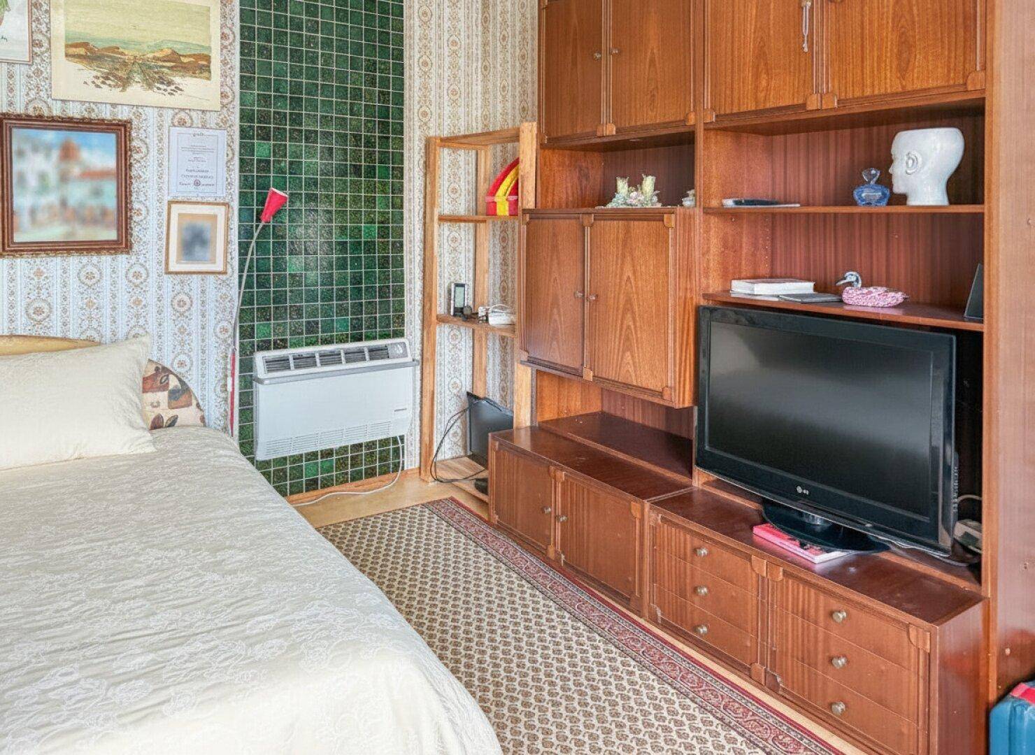 Schlafzimmer mit Bett, einer großen Holzwandverbauung inklusive Fernseher und gemusterter Tapete.