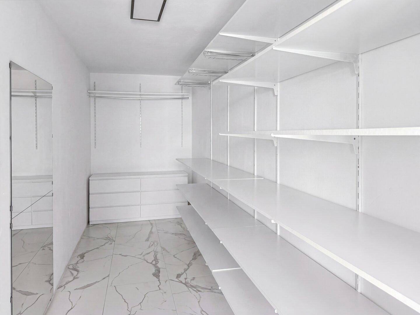 Geräumiger begehbarer Kleiderschrank mit weißen Regalsystemen und Schubladen.