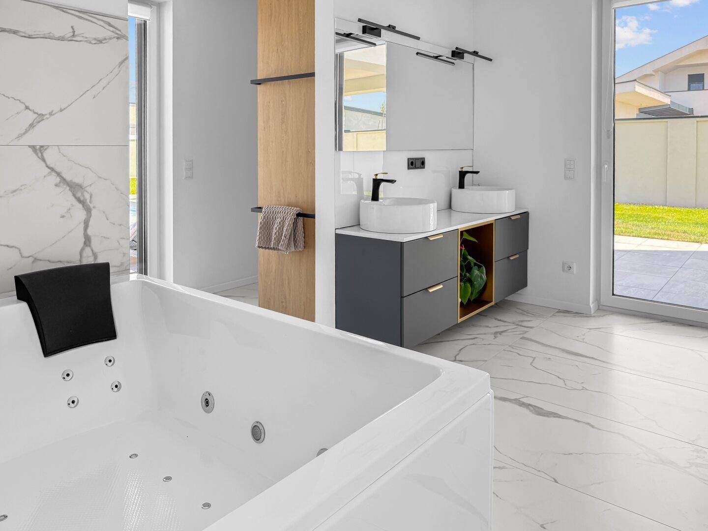 Luxuriöses Badezimmer mit Whirlpool, Doppelwaschbecken und großen Fenstern zum Garten.